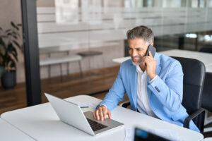 Busy happy mature business man talking on phone working on laptop in office.