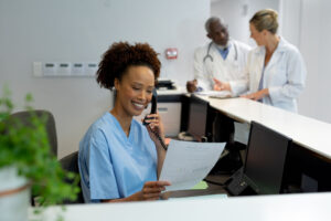 Mixed race female doctor at desk in hospital reception talking on phone and holding document. medicine, health and healthcare services.